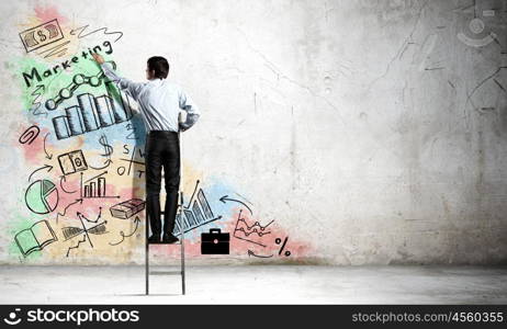 Business strategy and planning . Back view of businessman standing on ladder and drawing sketches on wall