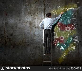 Business strategy and planning . Back view of businessman standing on ladder and drawing sketches on wall