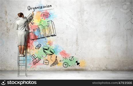 Business strategy and planning . Back view of businesswoman standing on ladder and drawing sketches on wall