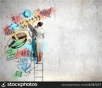 Business strategy and planning . Back view of businesswoman standing on ladder and drawing sketches on wall