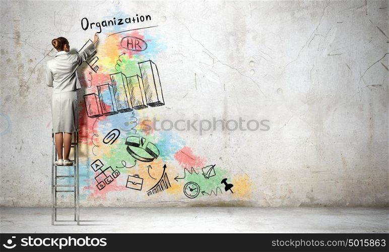 Business strategy planning. Back view of businesswoman standing on ladder and drawing sketch on wall