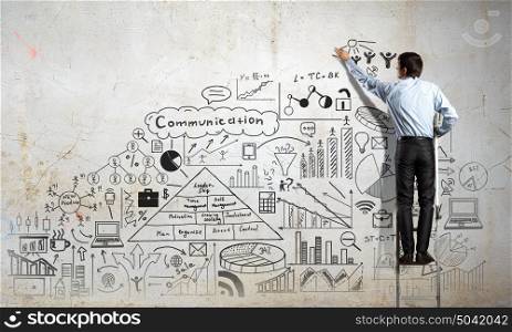Business strategy presentation. Back view of businessman standing on ladder and drawing his great plan on wall