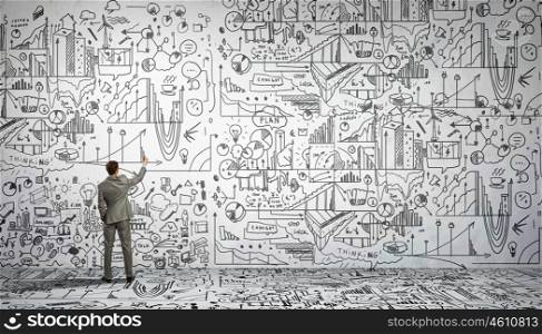 Business strategy. Rear view of businessman drawing business sketch on wall