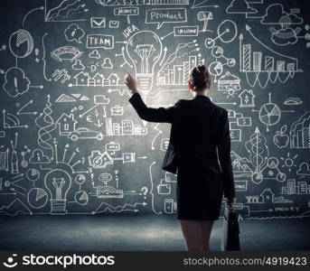 Business strategy. Rear view of businesswoman looking at business sketches on wall