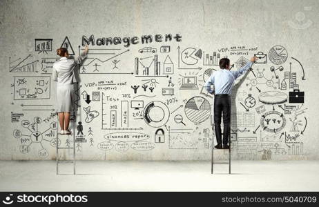 Business strategy seminar. Back view of businessman and businesswoman standing on ladder and drawing sketches on wall