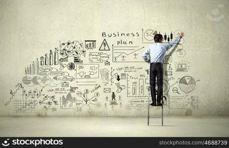 Business strategy seminar. Back view of businessman standing on ladder and drawing sketches on wall