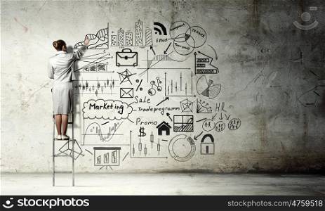 Business strategy seminar. Back view of businesswoman standing on ladder and drawing sketches on wall
