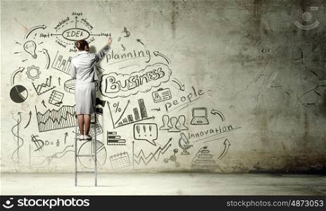 Business strategy seminar. Back view of businesswoman standing on ladder and drawing sketches on wall