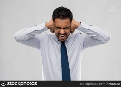 business, stress and people concept - screaming indian businessman covering ears with hands over grey background. screaming businessman covering ears with hands
