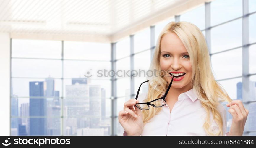 business, style and people concept - smiling businesswoman, student or secretary with eyeglasses over office window with city view background