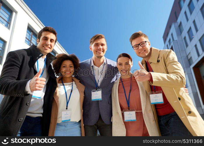 business, success and corporate concept - international group of people with name tags or conference badges showing thumbs up on city street. business team with conference badges in city
