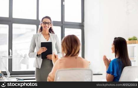 business, success and people concept - businesswomen applauding to colleague with tablet pc computer at office. business team applauding to woman at office. business team applauding to woman at office