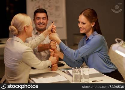 business, success and teamwork concept - happy coworkers making thumbs up gesture late at night office. business team making thumbs up gesture at office