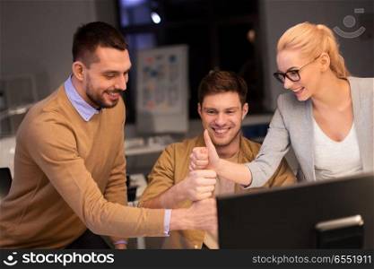 business, success and teamwork concept - happy coworkers with computer working late at night office making thumbs up gesture. business team making thumbs up gesture at office. business team making thumbs up gesture at office