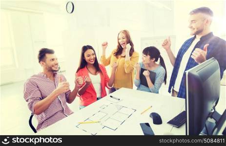 business, success, architecture, gesture and people concept - happy international creative architect team or students with blueprint celebrating triumph at office. happy creative team celebrating success at office. happy creative team celebrating success at office