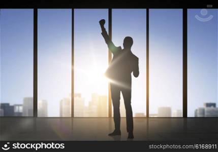 business, success, gesture and people concept - silhouette of happy businessman raising fist and celebrating victory over office window background