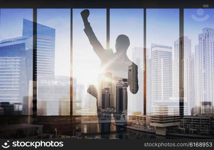 business, success, gesture and people concept - silhouette of happy businessman raising fist and celebrating victory over double exposure office and city background