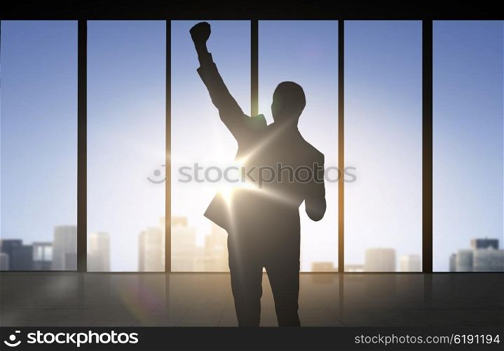 business, success, gesture and people concept - silhouette of happy businessman raising fist and celebrating victory over office window background