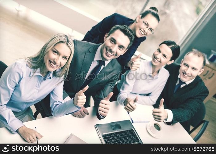business, success, technology and office concept - smiling business team with laptop computer, papers and coffee showing thumbs up in office