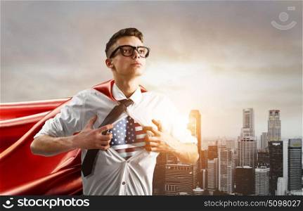 Business super hero. USA Superhero. Young businessman showing American flag under his shirt against sunset city.