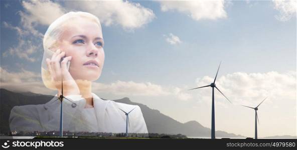 business, sustainable energy, technology and people concept - serious businesswoman with smartphone talking over wind turbines. businesswoman with smartphone over wind turbines