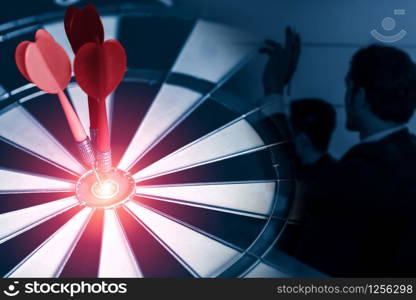 Business Target Goal For Success Strategy Concept - Red dart arrow hitting center goal on the dart board with business people working in background showing precision and success of business target.