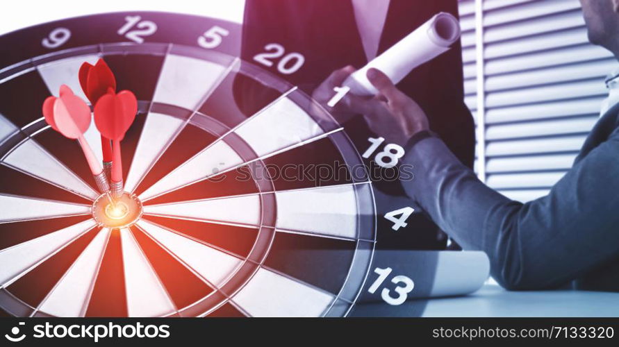 Business Target Goal For Success Strategy Concept - Red dart arrow hitting center goal on the dart board with business people working in background showing precision and success of business target.