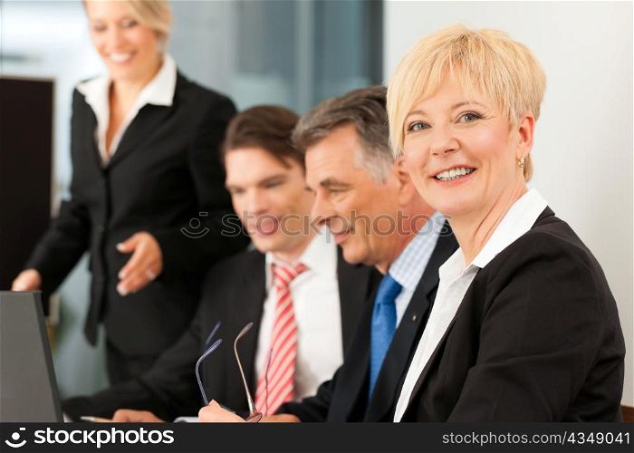 Business - team meeting in an office with laptop, the boss with his employees, one woman is looking into the camera