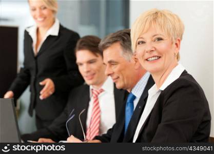Business - team meeting in an office with laptop, the boss with his employees, one woman is looking into the camera
