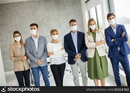 Business team members standing in the line with protective facial masks and looking at the camera in the office