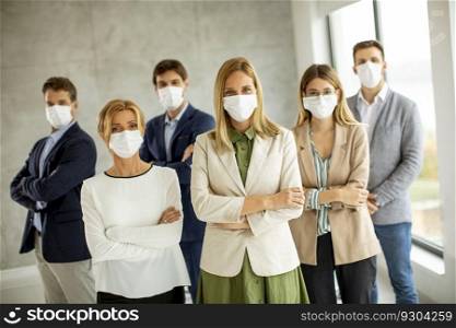Business team members standing with protective facial masks and looking at the camera in the office