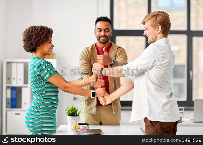 business, teamwork and corporate concept - happy creative team making thumbs up gesture at office. happy creative team making high five at office. happy creative team making high five at office
