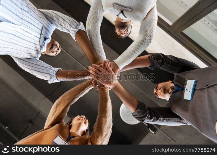 business, teamwork and corporate concept - happy smiling colleagues with name tags stacking hands at office. group of business people stacking hands at office