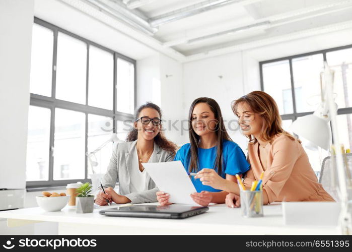 business, teamwork and people concept - female team or businesswomen discussing papers at office. businesswomen discussing papers at office. businesswomen discussing papers at office