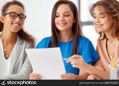 business, teamwork and people concept - female team or businesswomen discussing papers at office. businesswomen discussing papers at office. businesswomen discussing papers at office