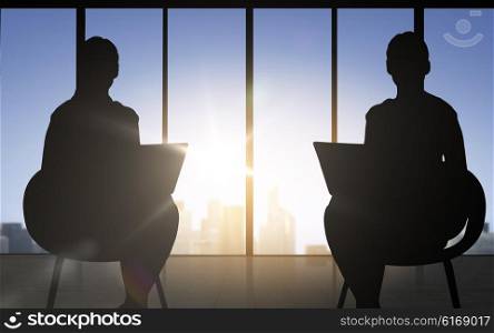 business, teamwork and people concept - silhouette of two women with laptop sitting on chair over office window background