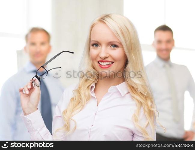 business, teamwork and people concept - smiling businesswoman, student or secretary with eyeglasses over office and group of colleagues background