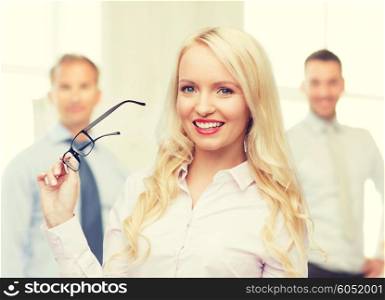 business, teamwork and people concept - smiling businesswoman, student or secretary with eyeglasses over office and group of colleagues background