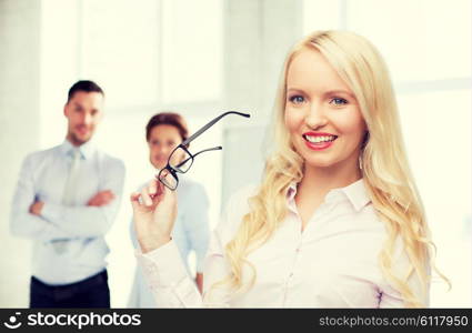 business, teamwork and people concept - smiling businesswoman, student or secretary with eyeglasses over office and group of colleagues background