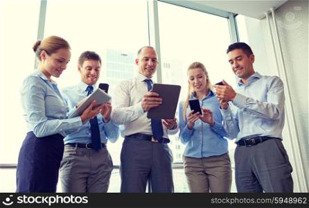 business, teamwork, people and technology concept - business team with tablet pc and smartphones meeting in office