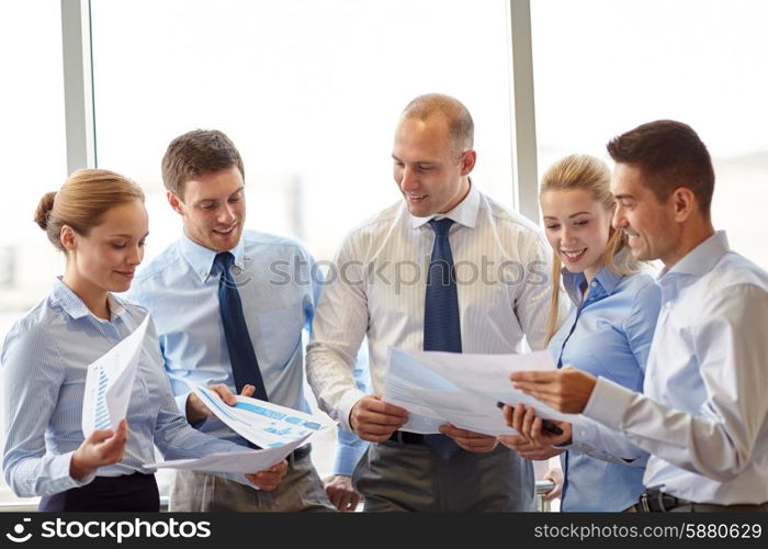 business, teamwork, people and technology concept - smiling business team with papers meeting and talking in office