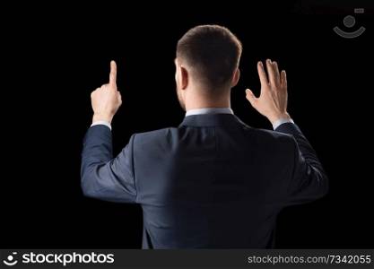 business, technology and augmented reality concept - businessman in suit working with invisible virtual screen over black background. businessman working with invisible virtual screen