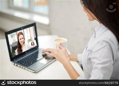 business, technology and communication concept - close up of businesswoman with laptop computer having video call with customer service operator and drinking coffee at office. woman drinking coffee having video call on laptop