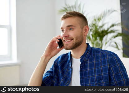 business, technology and communication concept - smiling young man calling on smartphone at office. smiling young man calling on smartphone at office