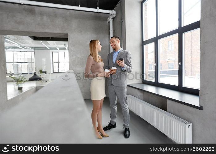 business, technology and corporate concept - happy smiling businesswoman and businessman with smartphone drinking coffee at office. businesswoman and businessman with smartphone