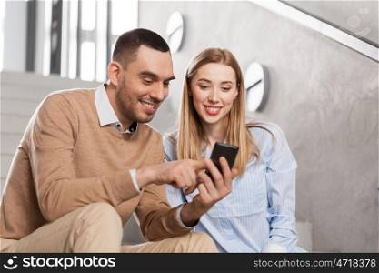 business, technology and corporate concept - smiling man and woman with smartphone at office stairs. man and woman with smartphone at office stairs. man and woman with smartphone at office stairs
