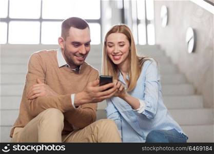 business, technology and corporate concept - smiling man and woman with smartphone at office stairs. man and woman with smartphone at office stairs