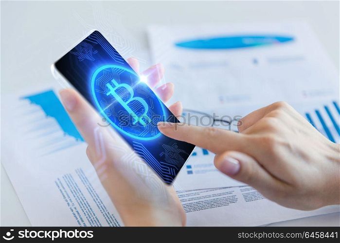 business, technology and cryptocurrency concept - close up of female hand holding smartphone with bitcoin hologram on screen. close up of hand with bitcoin on smartphone screen