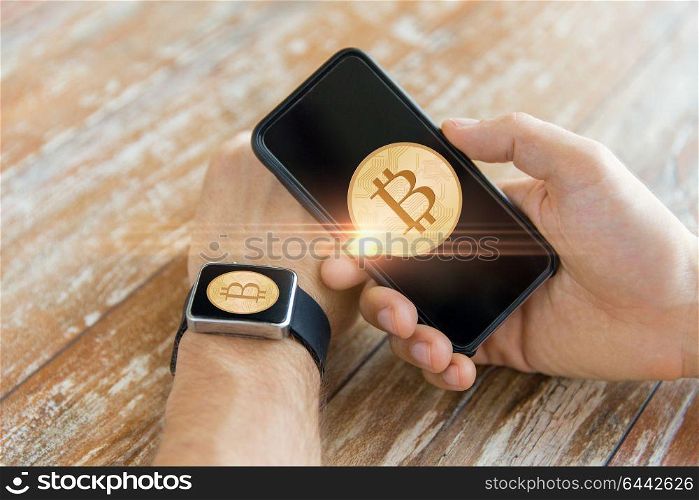 business, technology and cryptocurrency concept - close up of male hand holding smartphone and wearing smart watch with bitcoin on screen. close up of bitcoin on smartphone and smart watch