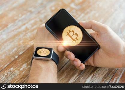 business, technology and cryptocurrency concept - close up of male hand holding smartphone and wearing smart watch with bitcoin on screen. close up of bitcoin on smartphone and smart watch